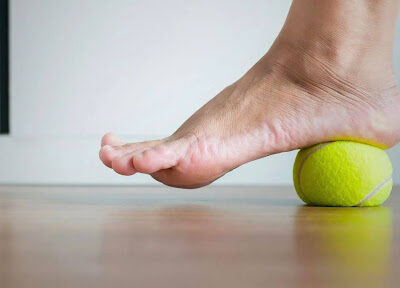 A person's foot applying pressure on a tennis ball to alleviate plantar fasciitis pain