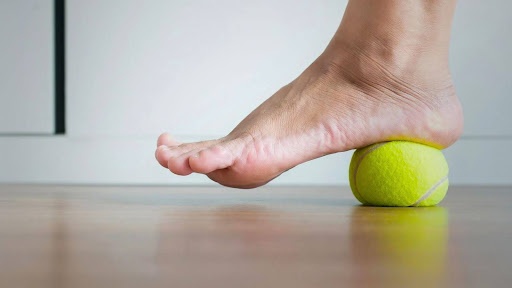 A person's foot applying pressure on a tennis ball to alleviate plantar fasciitis pain